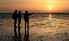 Drie silhouetten op het wad bij zonsopkomst